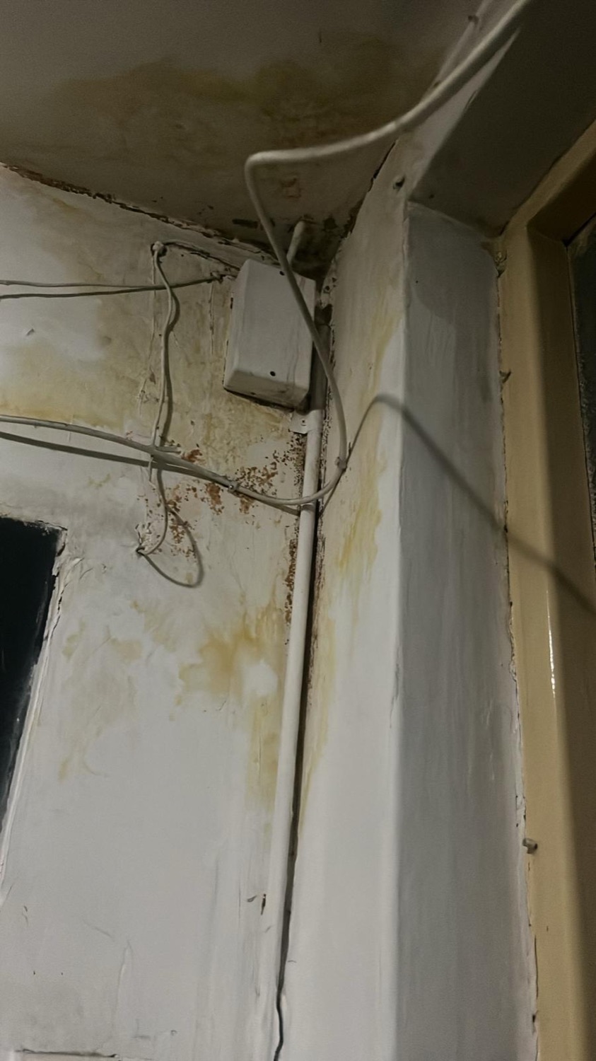 Perete cu infiltrații, tencuială căzută și instalație electrică veche, înainte de renovare
